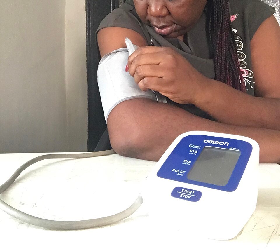 Woman checking for high blood pressure at home with an upper-arm cuff monitor